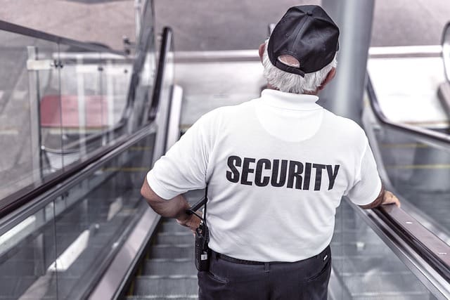 photo of a man wearing a shirt that reads security going down an escalator